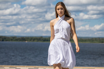 Young beautiful girl in a summer dress walking along the embankment