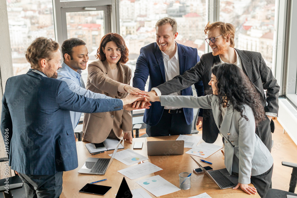 Aufkleber a diverse group of business professionals stand around a conference table, their hands stacked toget