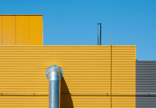 Yellow industrial building wall with duct and chimney