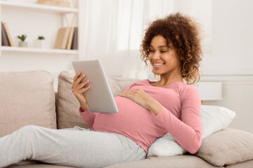 Fototapeta premium Order kids clothes. Happy pregnant girl using tablet, browsing internet at home