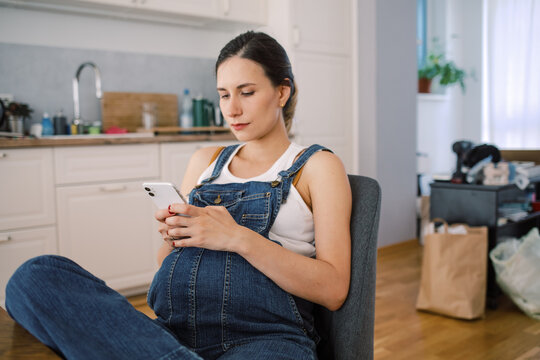 Pregnant Woman Relaxing with Smartphone in Kitchen