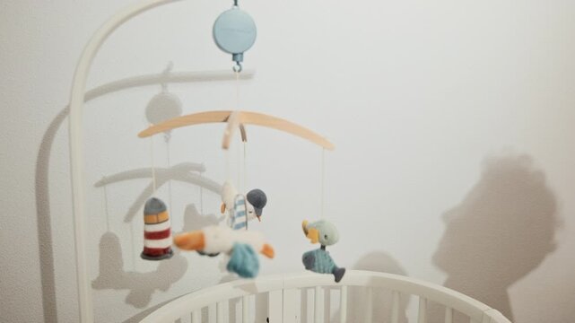 Silhouettes on white wall of the mother that playing with her little baby. Shadows near white cot with colourful crib mobile.