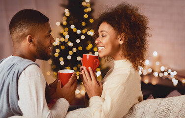 Afro couple drinking hot tea on Christmas eve, enjoying cozy evening at home