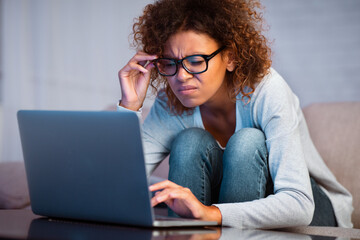 African-american student girl with bad eyesight using laptop, trying to make homework