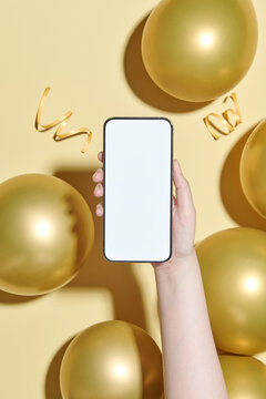 Mobile phone in hand over yellow confetti and balloons background