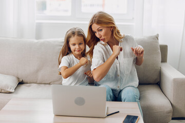 Joyful mother and daughter celebrating success while watching laptop on cozy living room couch