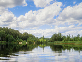 A lake with a cloudy sky in the background. The water is calm and the sky is bright and cloudy. Summer season time. Nature scene. Calm and relaxing mood. Good swimming area with clean water.