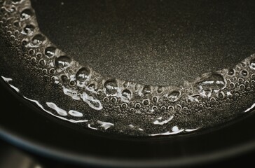 boiling water with macro bubbles close-up on black kitchen stove for cooking