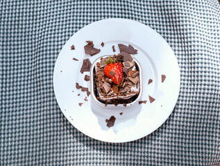 Chocolate cake and chocolate flakes. A very typical chocolate layered cake at bakery or pastry shop. A sugar coated strawberry for decoration. Good concept for outdoor birthday in nice weather