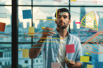 Portrait of young handsome businessman writing marketing idea by using colorful marker on glass...