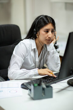 Woman with headset in office in front of computer looking bored