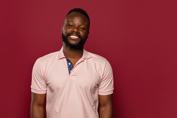 Smiling black man in pink polo shirt posing against red background