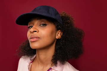 Confident woman in navy cap on red background looks at camera