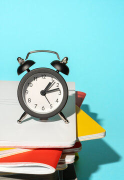 Black alarm clock on stacked notebooks against blue background.