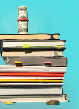 Rolled dollar bill on set of various notebooks with colorful bookmarks