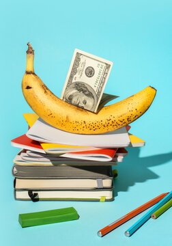 One hundred dollar bill on banana and notebooks on blue background.