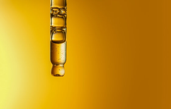 Clear glass pipette with face serum on yellow and orange background