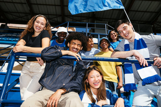 Group of friends having fun and cheering with flag at stadium