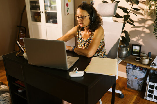 middle aged woman working in home office with bluetooth headset 