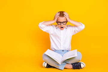 Photo of clever funny charming boy wear white shirt sit floor read book encyclopedia isolated on yellow color background