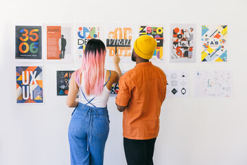 Man and woman analyzing creative posters on a white wall