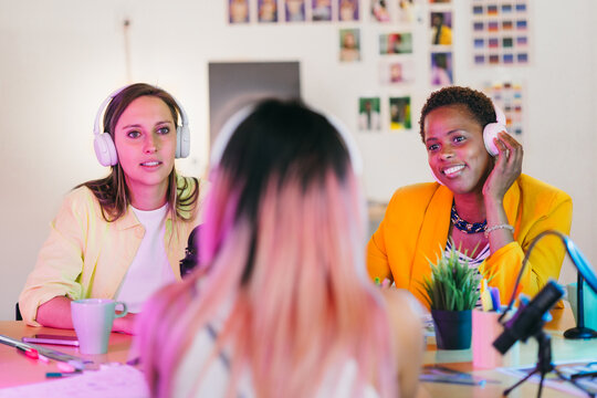 Diverse women recording podcast in modern studio with colorful lights