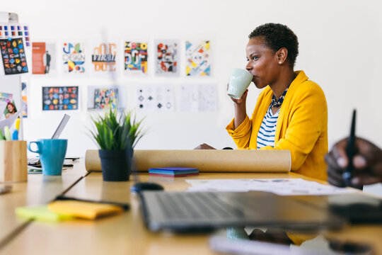 Creative black woman drinking coffee while working in a modern office