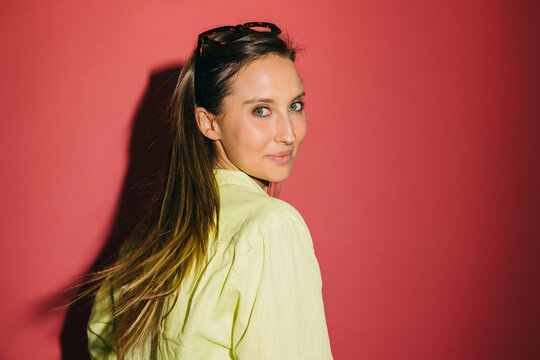 Smiling woman in yellow shirt with sunglasses posing over red wall