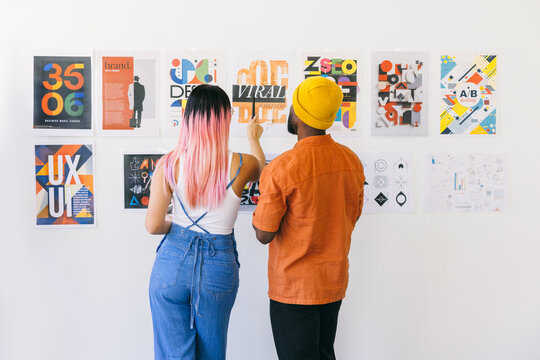 Man and woman analyzing creative posters on a white wall