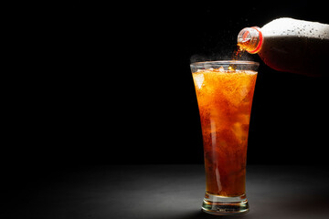 Black soda. Close-up of pouring soda with ice in a glass. Placed on a black and dark background.