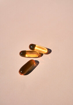Three Golden Omega 3 Capsules under Sunlight on Beige Background. 