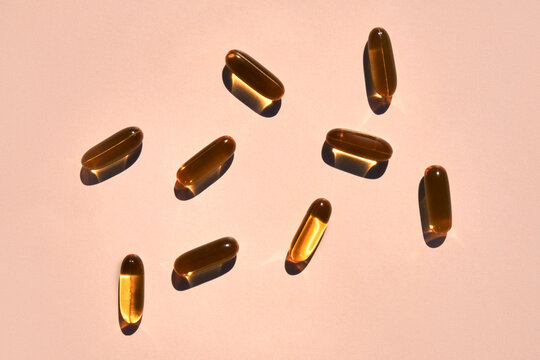 Many Golden Omega 3 Capsules under Sunlight on Beige Background. 
