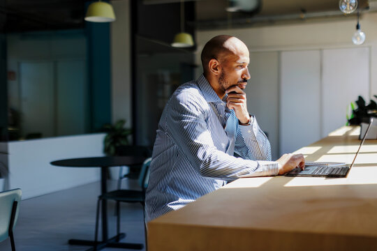 Thoughtful businessman working on laptop in modern office