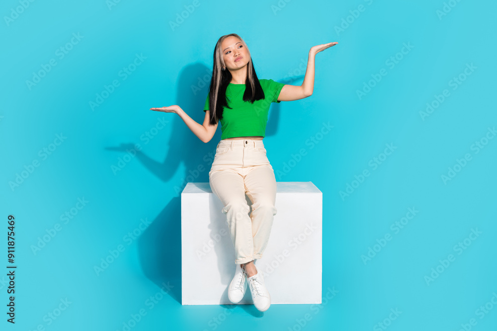 Wall mural Full body portrait of pretty young girl sit cube hold empty space wear t-shirt isolated on turquoise color background