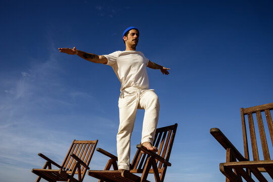 Man Balancing on Chairs Against a Blue Sky
