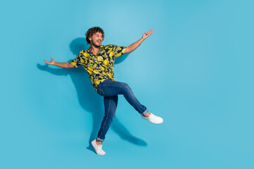 Fototapeta premium Full size photo of positive man dressed print shirt jeans raising arms up dancing look empty space isolated on blue color background