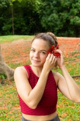 Fototapeta premium Portrait of beautiful latin hispanic woman putting a flamboyant red flower behind her ear in the outdoors. Springtime morning concept.