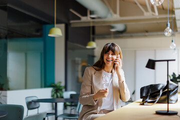 Happy businesswoman talking on phone in modern office space