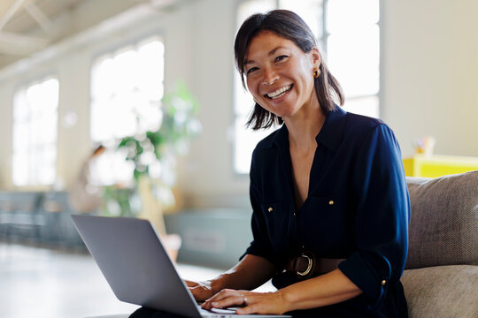 Smiling corporate businesswoman working on laptop in modern office - Powered by Adobe