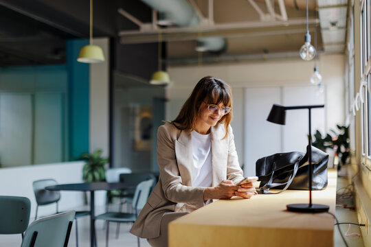 Businesswoman using smartphone in modern office cafeteria