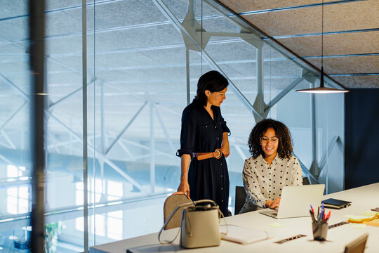 Female colleagues collaborating using laptop in modern office - Powered by Adobe