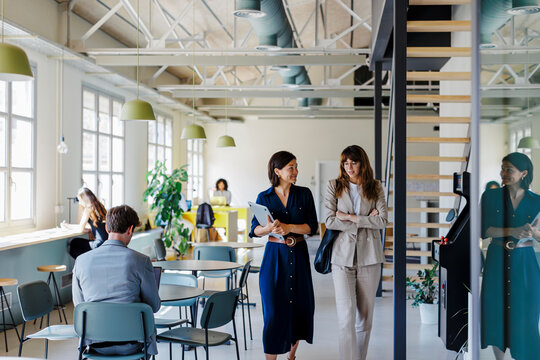 Female coworkers walking and talking in busy open plan office - Powered by Adobe
