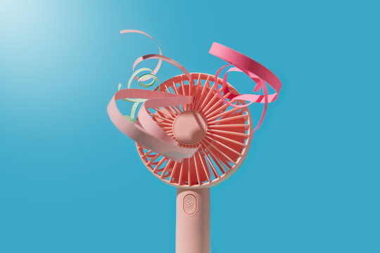 Pink fan with ribbons fluttering into camera over blue background
