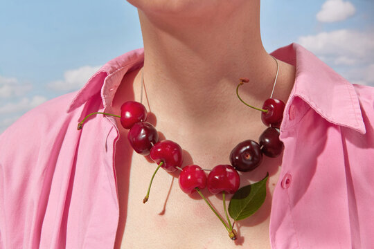 Person wearing pink shirt and necklace with silver lace and cherries