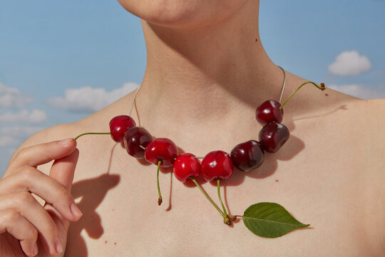 Human holding tail of cherries hanging in row on chain around neck