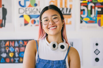 Smiling asian young woman with headphones in a creative workspace