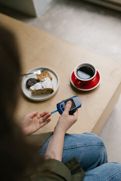 Glucose meter, cup of coffee and deserts. Woman measuring sugar level