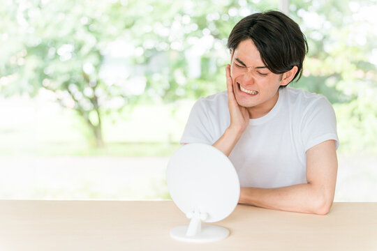鏡を見ながら虫歯・歯列矯正・歯周病・歯が気になる若い男性（歯痛）
