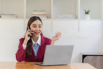 Business women in the office use smartphones to send online messages and talk with customers on the phone and use laptops to conduct financial business online, discuss and contact customers.