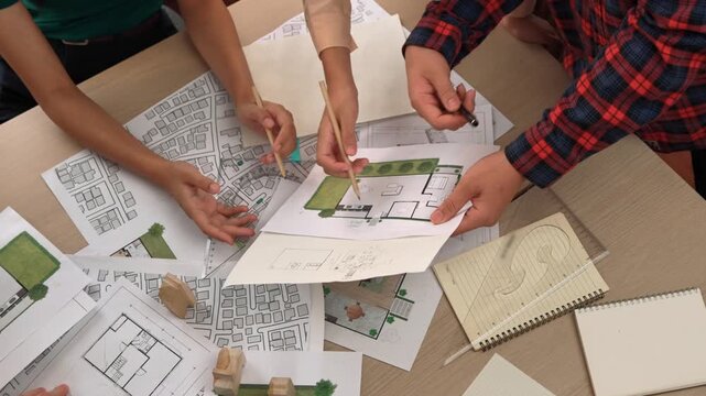 Smart architect and safety engineer discussion about building blueprint on table with architectural document, measurement tools and wooden block scatter around at modern office. Closeup. Delineation.